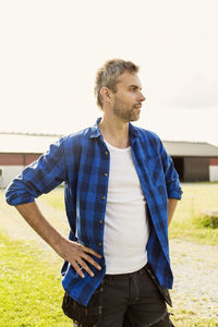 Mature man looking away while standing with hand on hip at farm