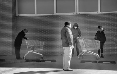 People wearing masks with shopping carts against building