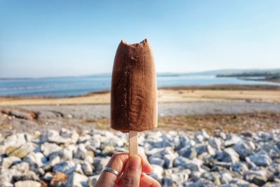 Cropped hand holding ice cream cone on beach against clear sky