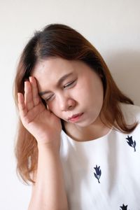 Young woman suffering from headache against white wall