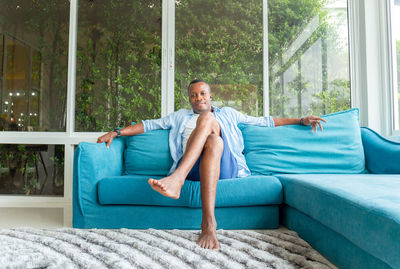 Full length portrait of a young man sitting on sofa