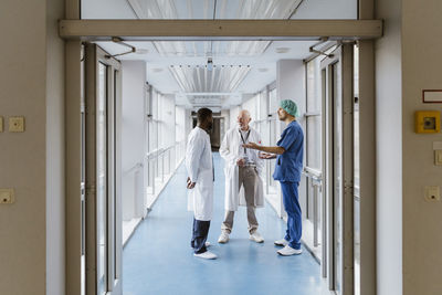 Full length of physician and doctors discussing while standing in corridor at hospital