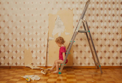 Child tear off the wallpaper from the wall in the room, little mother's helper