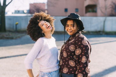 Young woman smiling while standing with cheerful friend on footpath