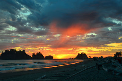 Scenic view of beach against dramatic sky during sunset