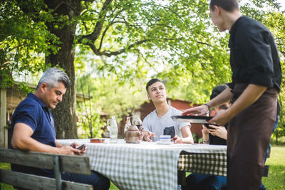 Teenage boy looking at waiter while sitting with friends in restaurant