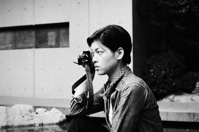 Portrait of young man holding camera while sitting outdoors