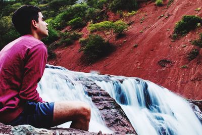 Man sitting against waterfall at forest