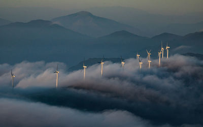 High angle view of windmills against silhouette mountains during foggy weather