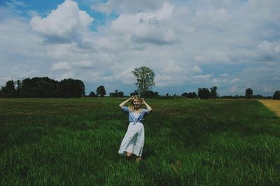 Portrait of woman standing on grassy land against cloudy sky