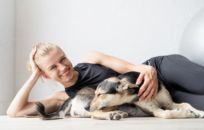 Young sportive woman embracing her mixed breed dog laying on the floorat home