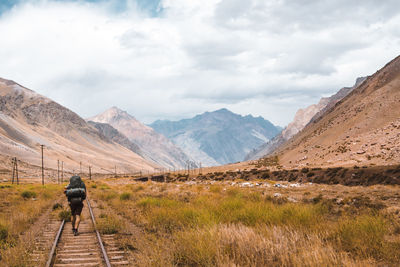 Rear view of man walking on railroad track against mountain