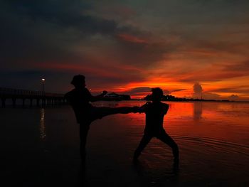 Silhouette people standing against orange sky during sunset