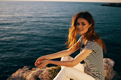 Young woman sitting on rock by sea