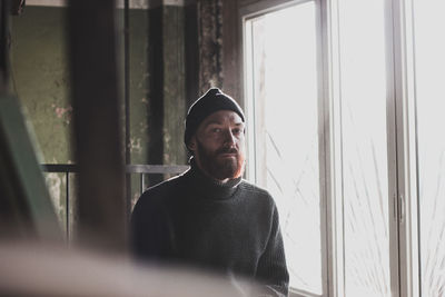 Portrait of man wearing hat standing against window