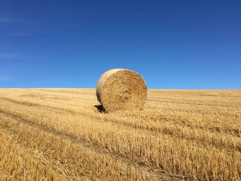 Hay bales on field against clear blue sky