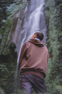 Rear view of man standing in forest against waterfall