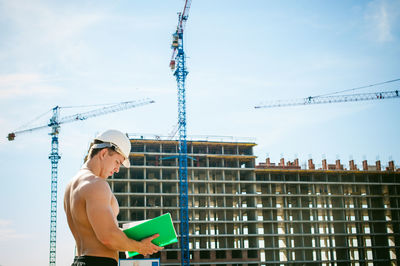 Shirtless man standing against construction buildings