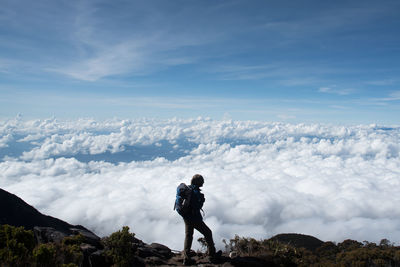 Hiker standing on mountain against cloudscape