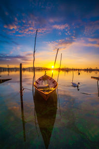 Fishing boats moored in sea against sky during sunset
