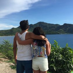 Rear view of couple standing by lake against sky