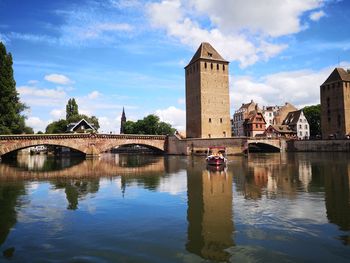 Arch bridge over river by buildings against sky