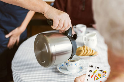 Midsection of female caretaker pouring coffee for senior couple at home