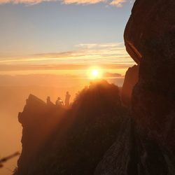 Silhouette people looking at rock formation against sky during sunset