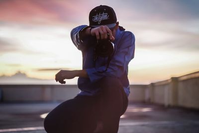 Full length of man holding camera while standing against sky