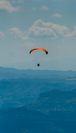 Person paragliding over mountain against sky