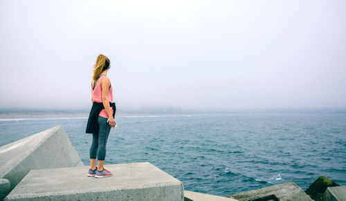 Rear view of woman standing by sea against clear sky