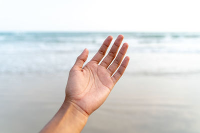 Close-up of hand against sea against sky