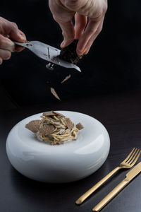 Hands of crop anonymous chef grating delicious black truffles on pasta served in white plate near cutlery in modern restaurant