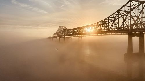 Illuminated bridge over river against sky during sunset