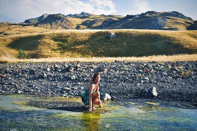 Woman at riverbank against mountains