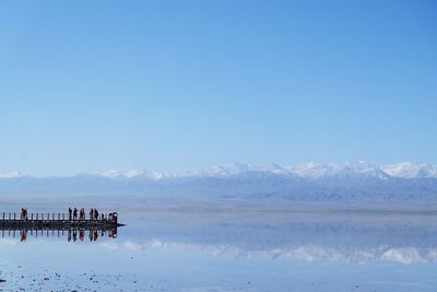 People on lake against clear blue sky