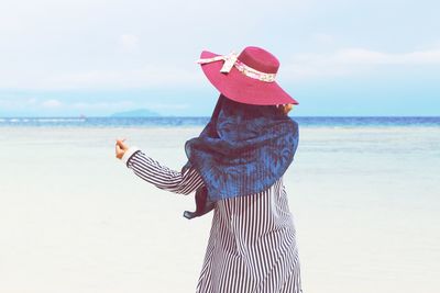 Rear view of woman wearing hat while standing at beach