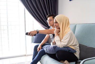 Couple watching tv while sitting on sofa at home