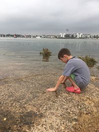 Boy crouching at beach against sky