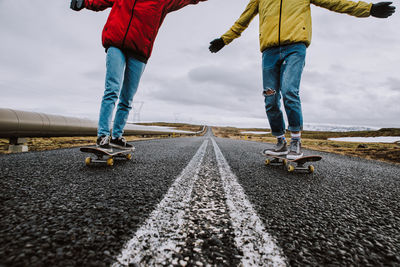 Lows section of couple skateboarding on road against sky