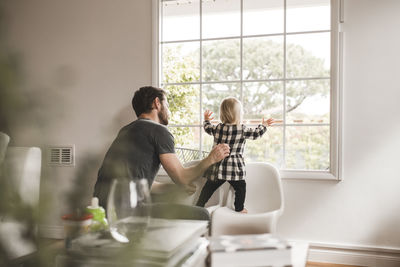 Mid adult man with daughter looking through window at home