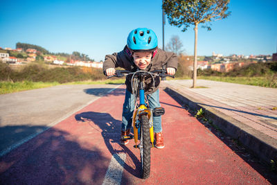 Boy riding bicycle on road in city during sunny day