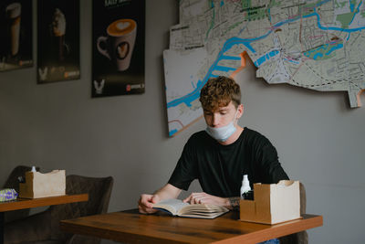 A student guy is sitting at a table in a cafe, studying educational material, reading a book 