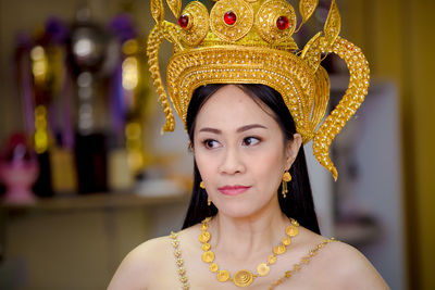 Mature woman wearing golden crown and jewelries looking away at home