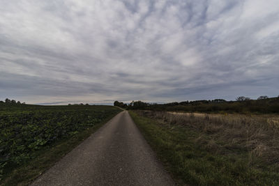 Empty road amidst field against sky