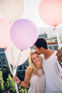 Couple standing with balloons against sky