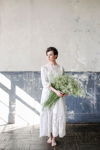 Beautiful young woman holding plant standing at home