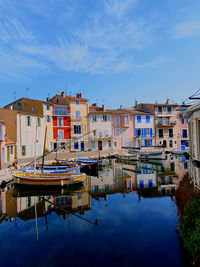 Sailboats moored on lake by buildings in city against sky