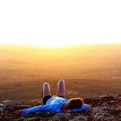 Woman sleeping on cliff against clear sky