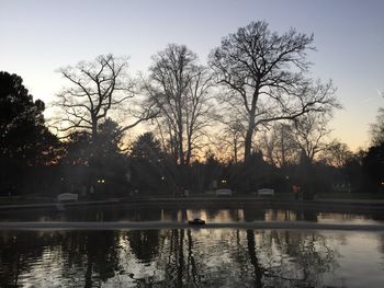 Silhouette bare trees in front of lake against sky during sunset